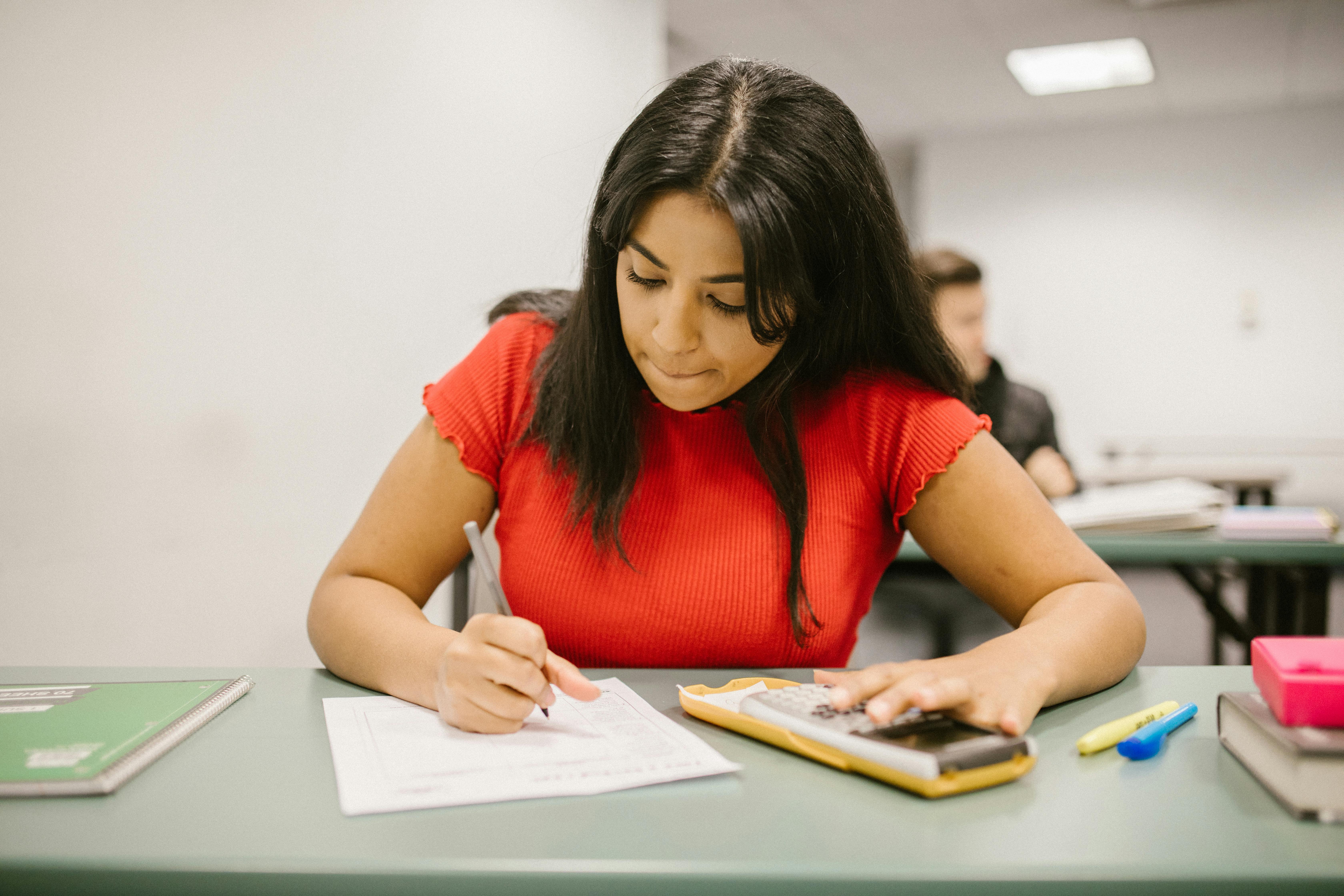 Teenage South Asian girl in red using a calculator while taking a maths test.