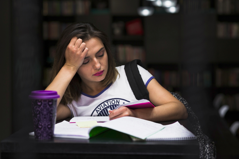 Teenage girl studying late at a library desk reading an open book.