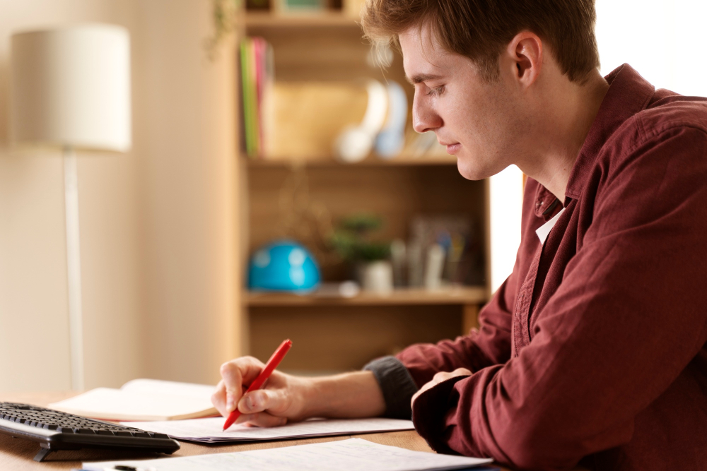A teenage boy in a red shirt studying at his desk.