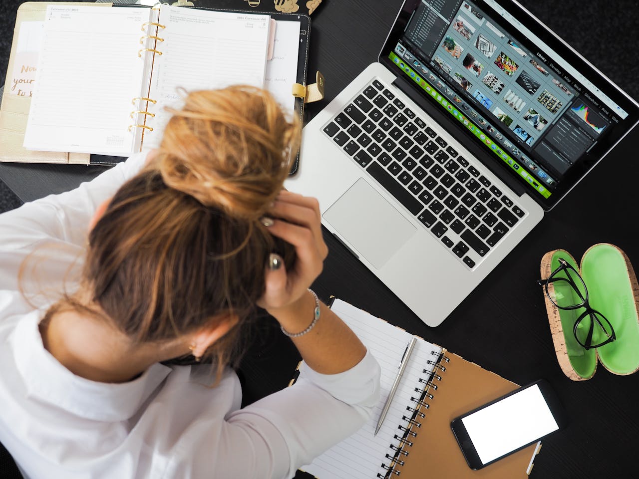 Teenage girl sitting at a desk with MacBook, holding her head in her hands, looking stressed.