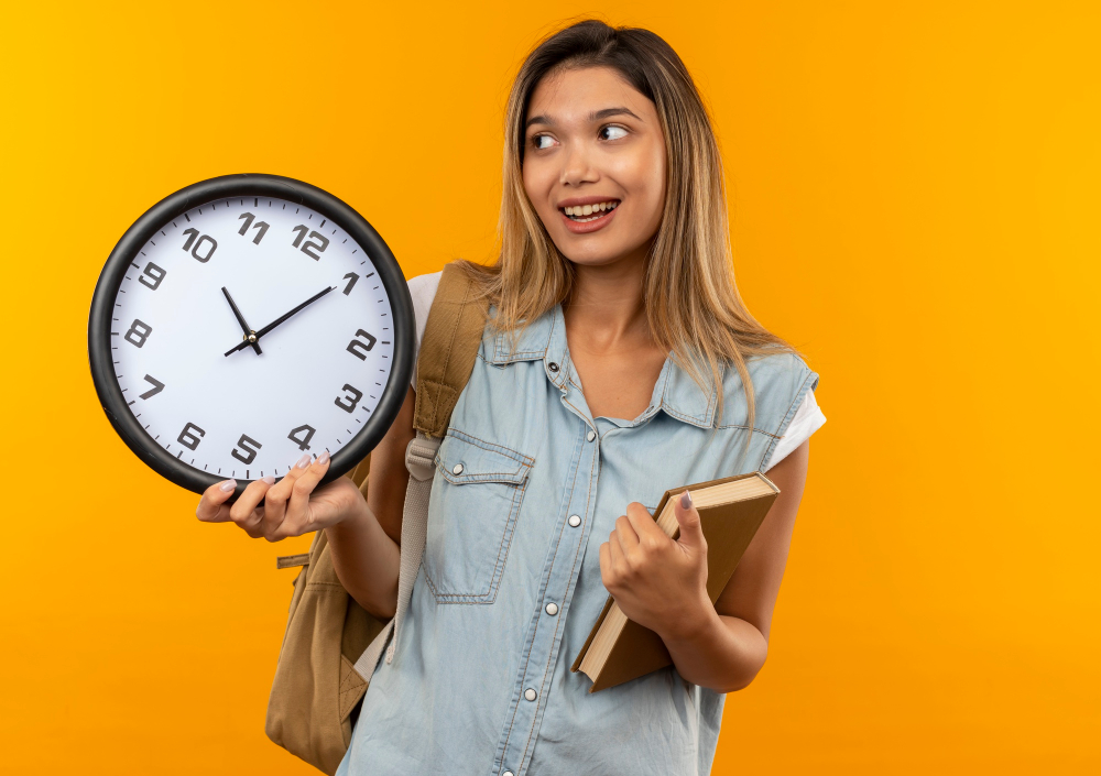 Young female student holding a clock and a book, wearing a backpack.